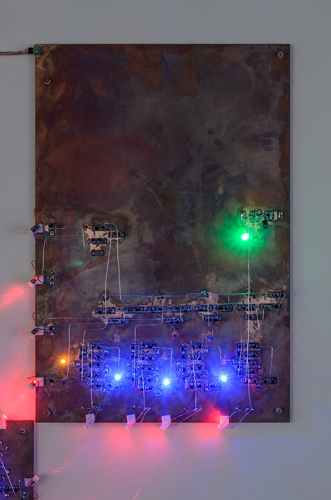 A plate of copper with shining blue, yellow and green LEDs on it. There are structures made of transistors engraved into the the bottom hal of its surface.