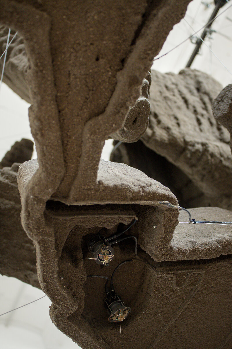A detail shot of one of the structures inside the cube. It is made from earth and consists of multiple layers stacked on top of each other. A small machine is sitting within a depression.
