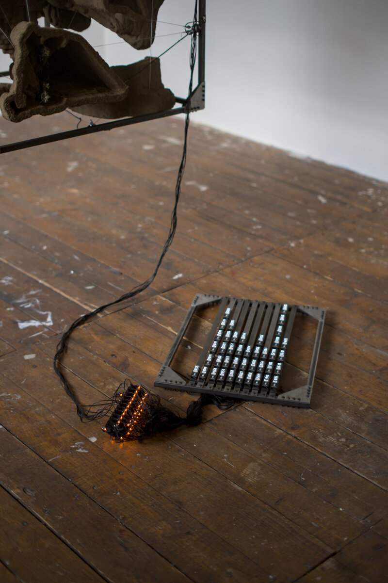 A detail of the metal frame and the black structure. The suspended frame is connected via black cable to the machine.