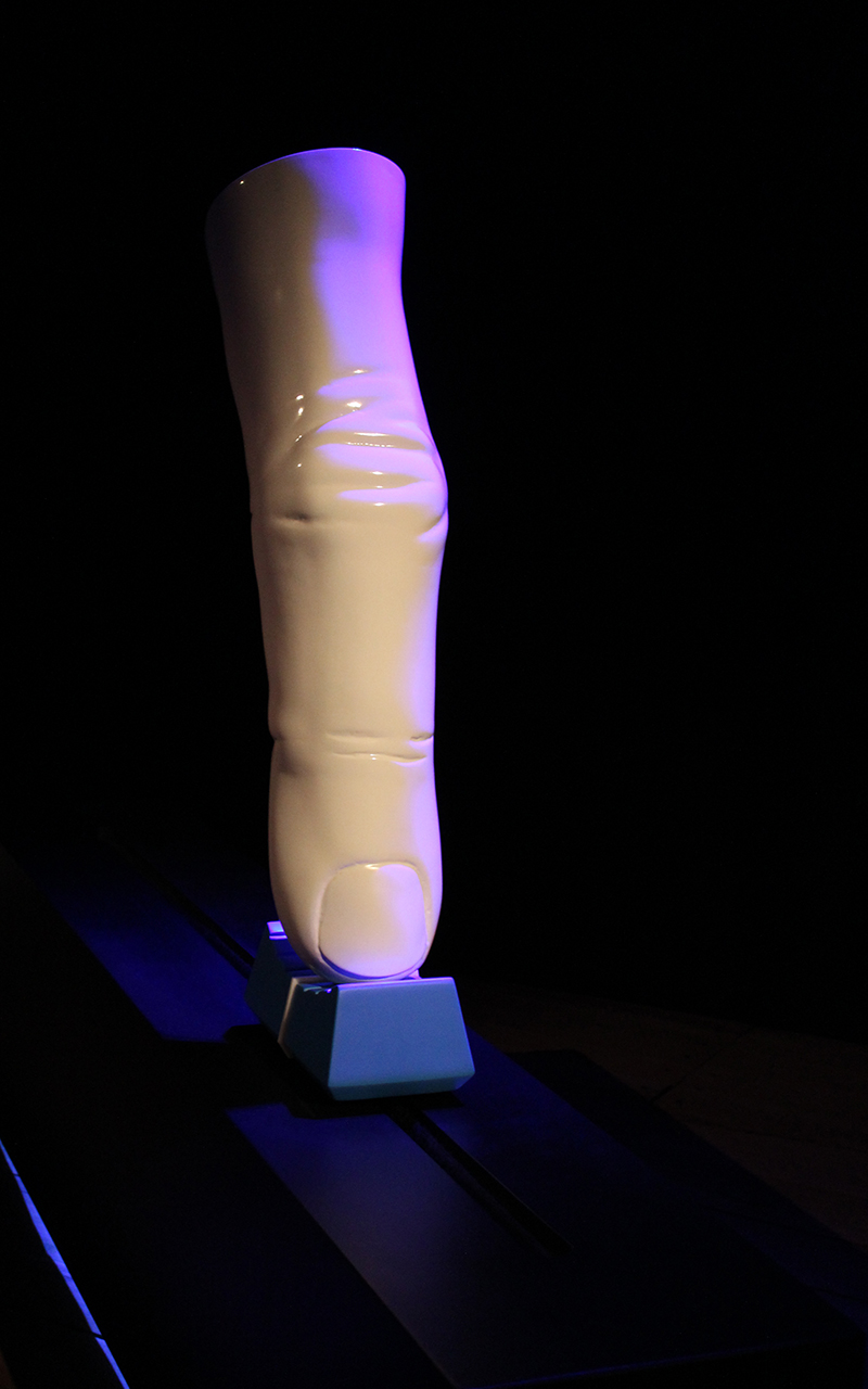 A large finger. It is white and shiny, looking like it is made from porcellain. It sits on top of an oversized blue fader cap.