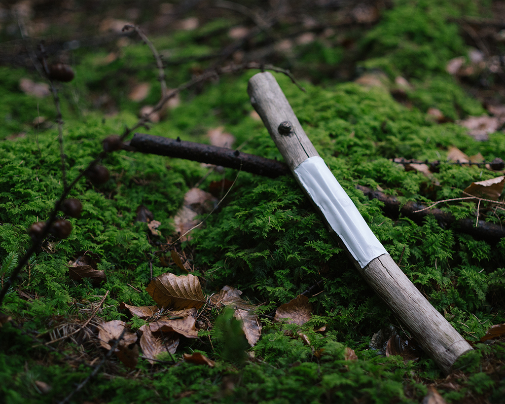 A piece of a branch lies on a mossy, green forest floor. Its middle piece has been replaced by some kind of grey plastics.
